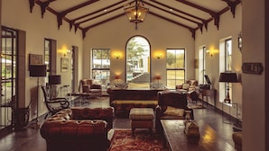 A spacious living room with a high ceiling, leather sofas, a large rug, and a view through an arched doorway to an outdoor area. - Kili Seasons Hotel (Arusha)