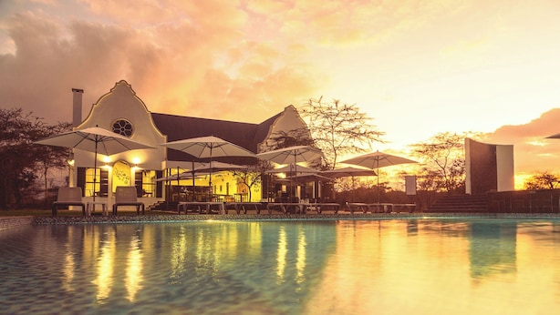 A poolside area with lounge chairs and umbrellas, a building with a distinctive architectural design, and a sunset sky. - Kili Seasons Hotel (Arusha)
