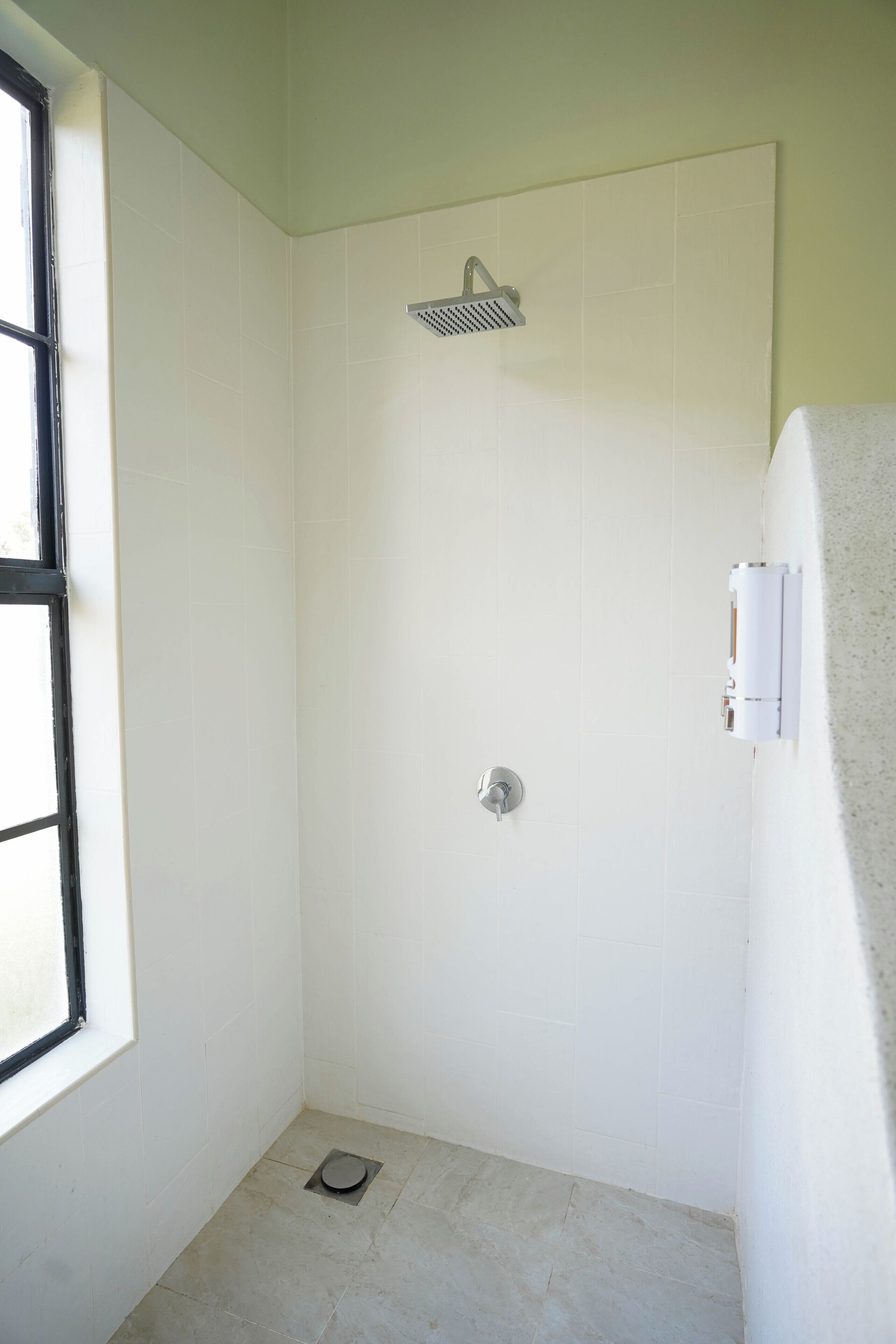 A small, white-tiled bathroom with a shower, a window, and a towel rack.