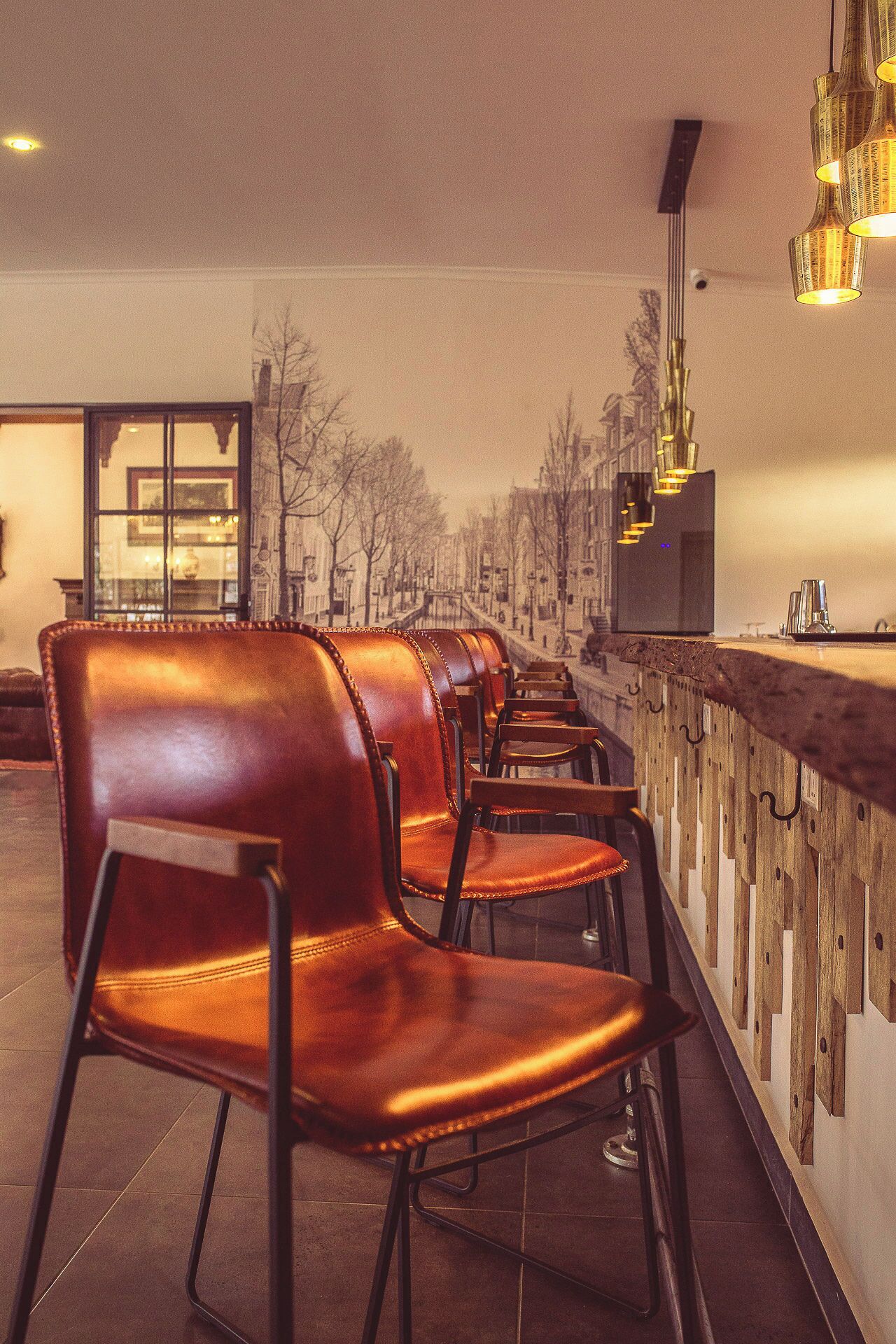 A row of leather chairs with metal frames, a wooden counter, and hanging pendant lights in a cafe setting.