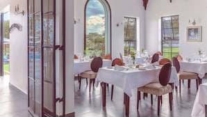 A dining area with tables set for a meal, large windows with a view of the outdoors, and a door leading outside. - Kili Seasons Hotel (Arusha)