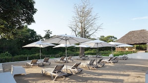 A beachside lounge area with sun loungers and umbrellas, surrounded by trees and a thatched-roof structure. - Kili Seasons Hotel (Arusha)