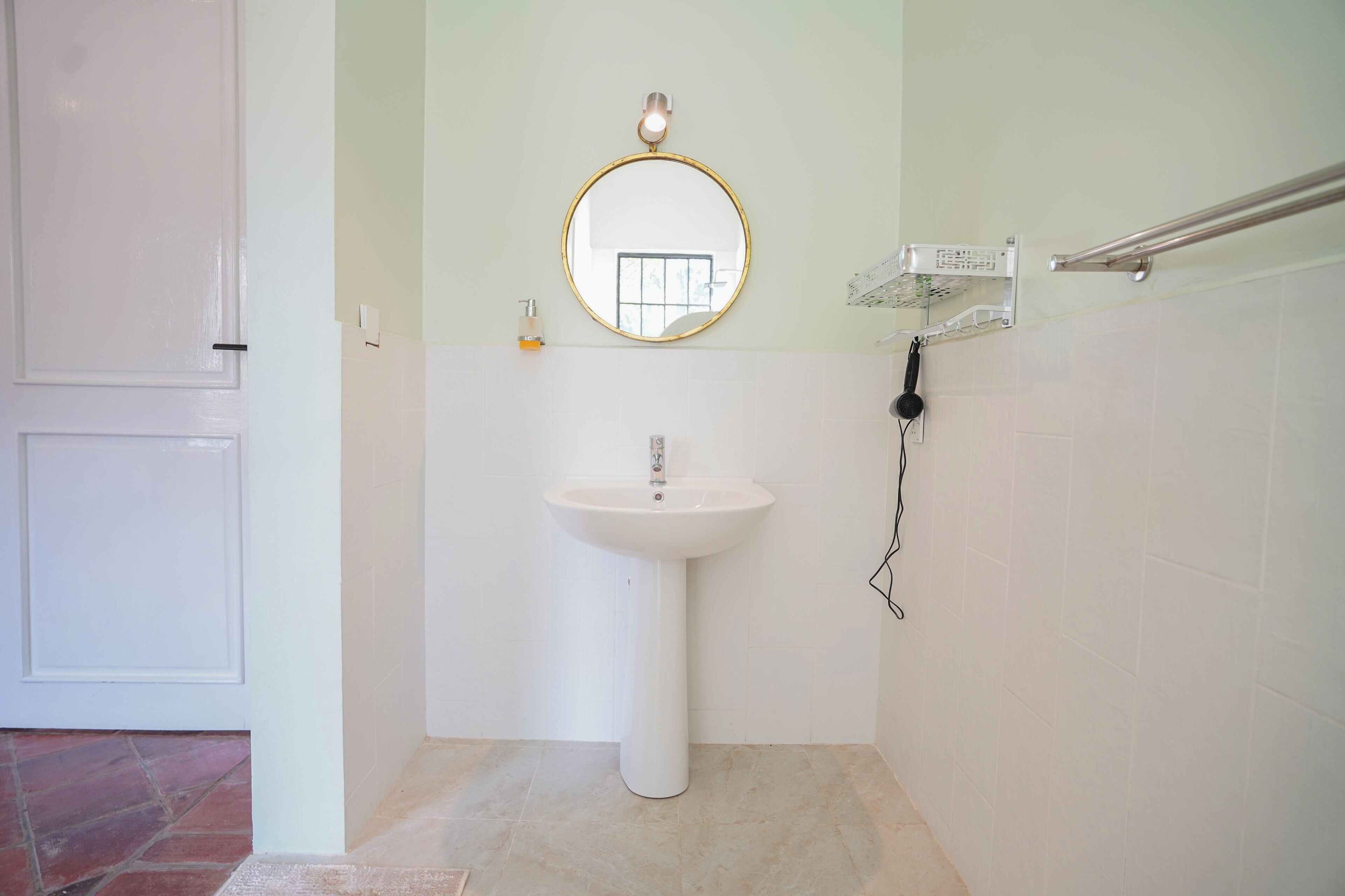 A bathroom with a pedestal sink, a round mirror, a towel rack, and a hand sanitizer dispenser.