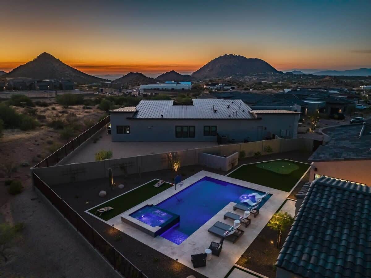 Una moderna casa con piscina, patio e vista sulle montagne al tramonto.