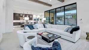 Un salon moderne avec un canapé d’angle, une table basse et une vue sur la cuisine et l’extérieur.