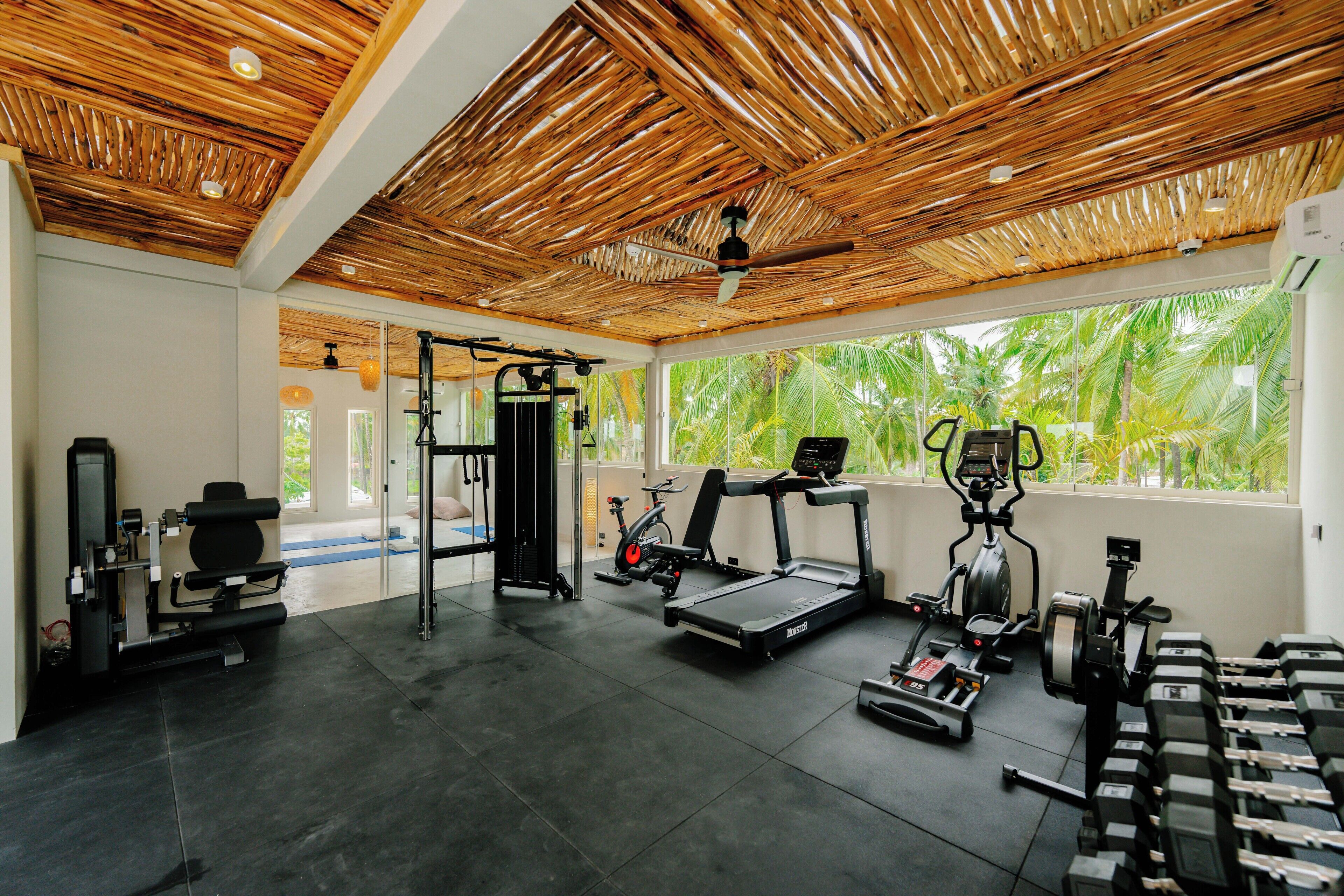 A gym with exercise equipment, large windows, and a wooden ceiling.