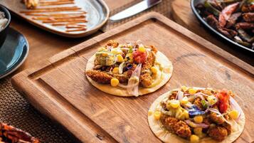 Un tavolo di legno con diversi piatti, tra cui tacos e gamberi, e un bicchiere di bevanda rossa.
