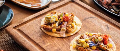 A wooden table with various dishes, including tacos and shrimp, and a glass of red drink.