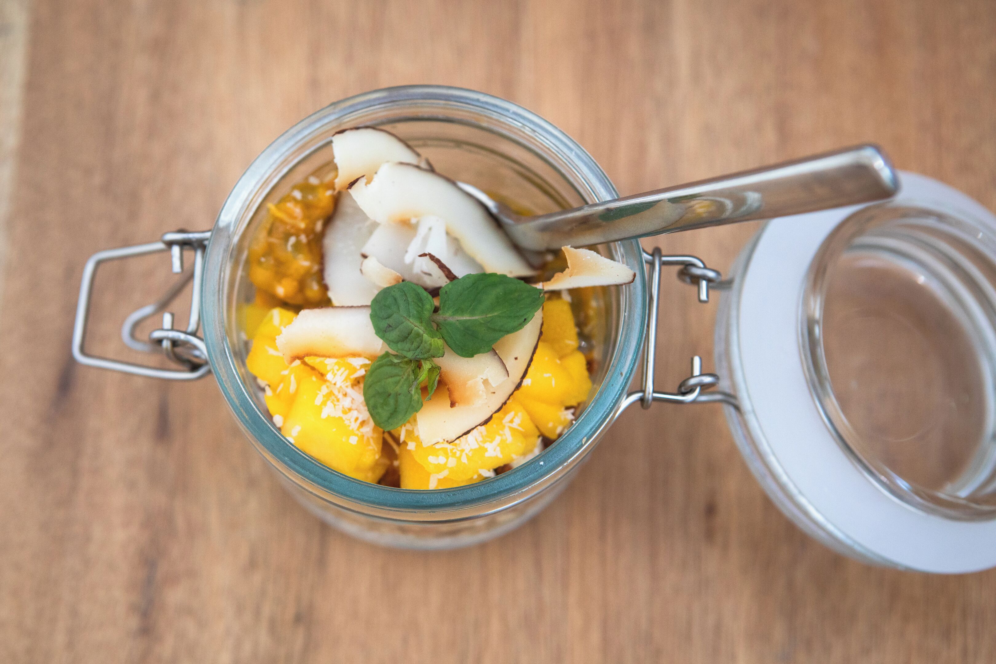 A glass jar with a metal clasp lid containing sliced mango and coconut pieces, garnished with mint leaves.