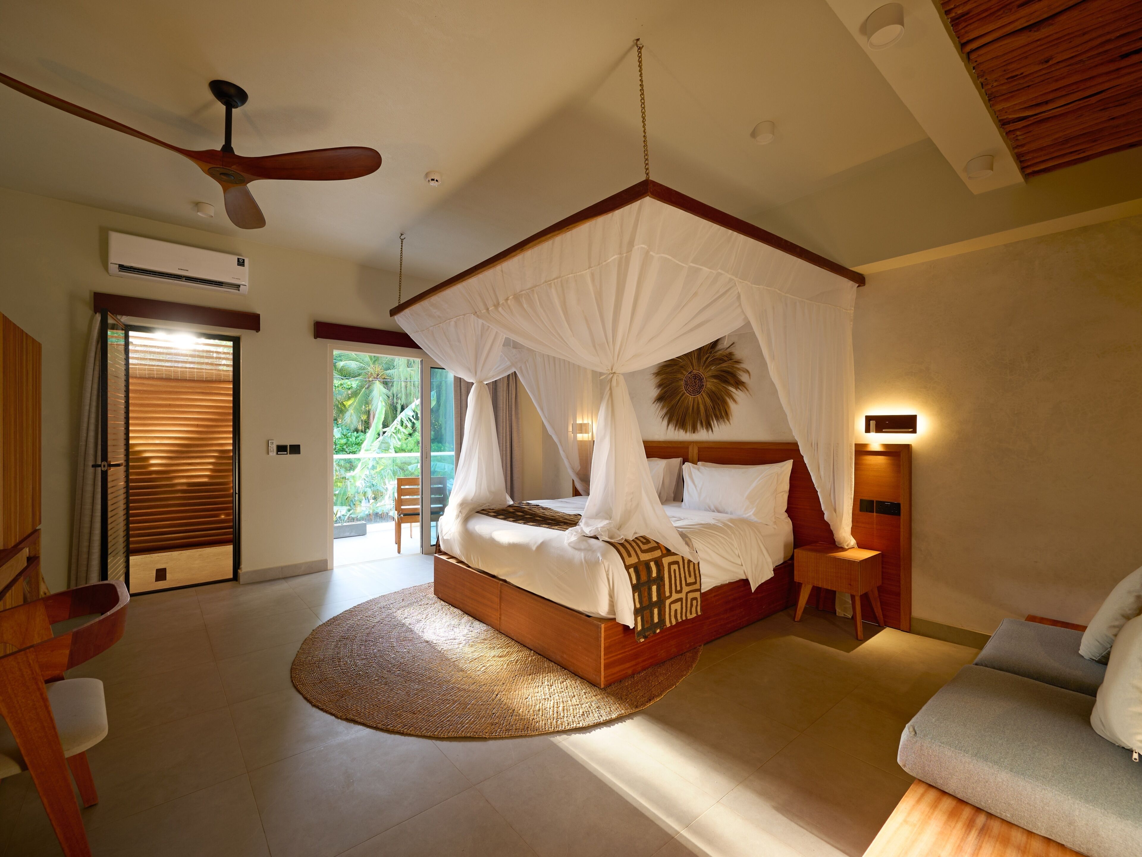 A bedroom with a four-poster bed, a ceiling fan, a large window, and a wooden floor.