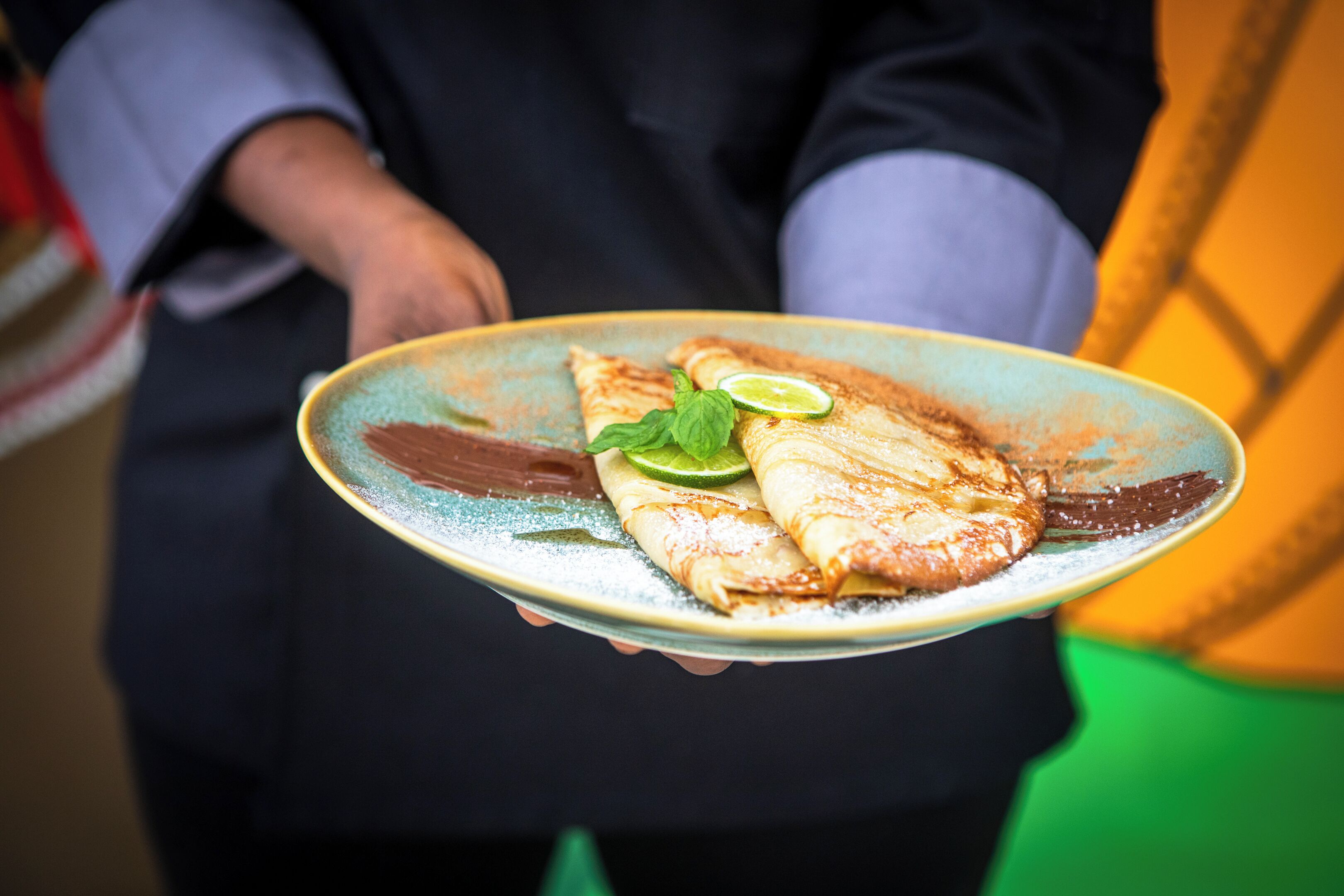A person holding a plate with a fish fillet, lime, and mint leaves.