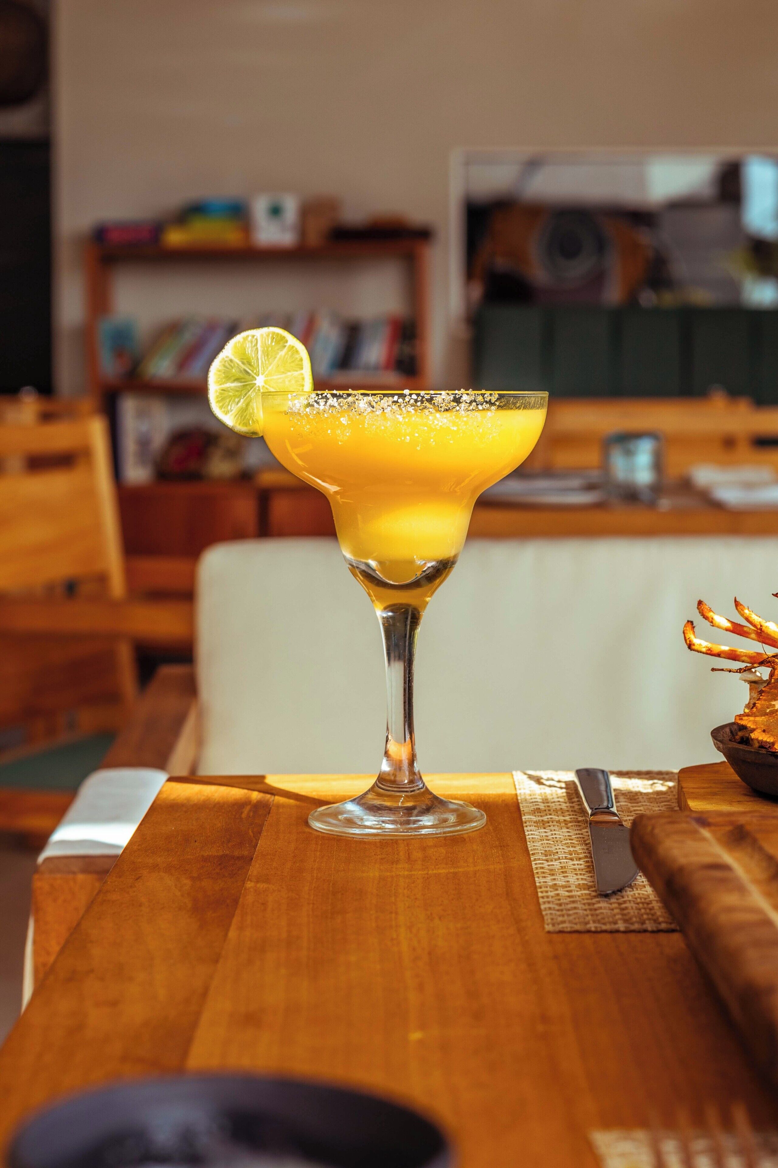 Un cóctel en un vaso con una cuña de lima sobre una mesa de madera.