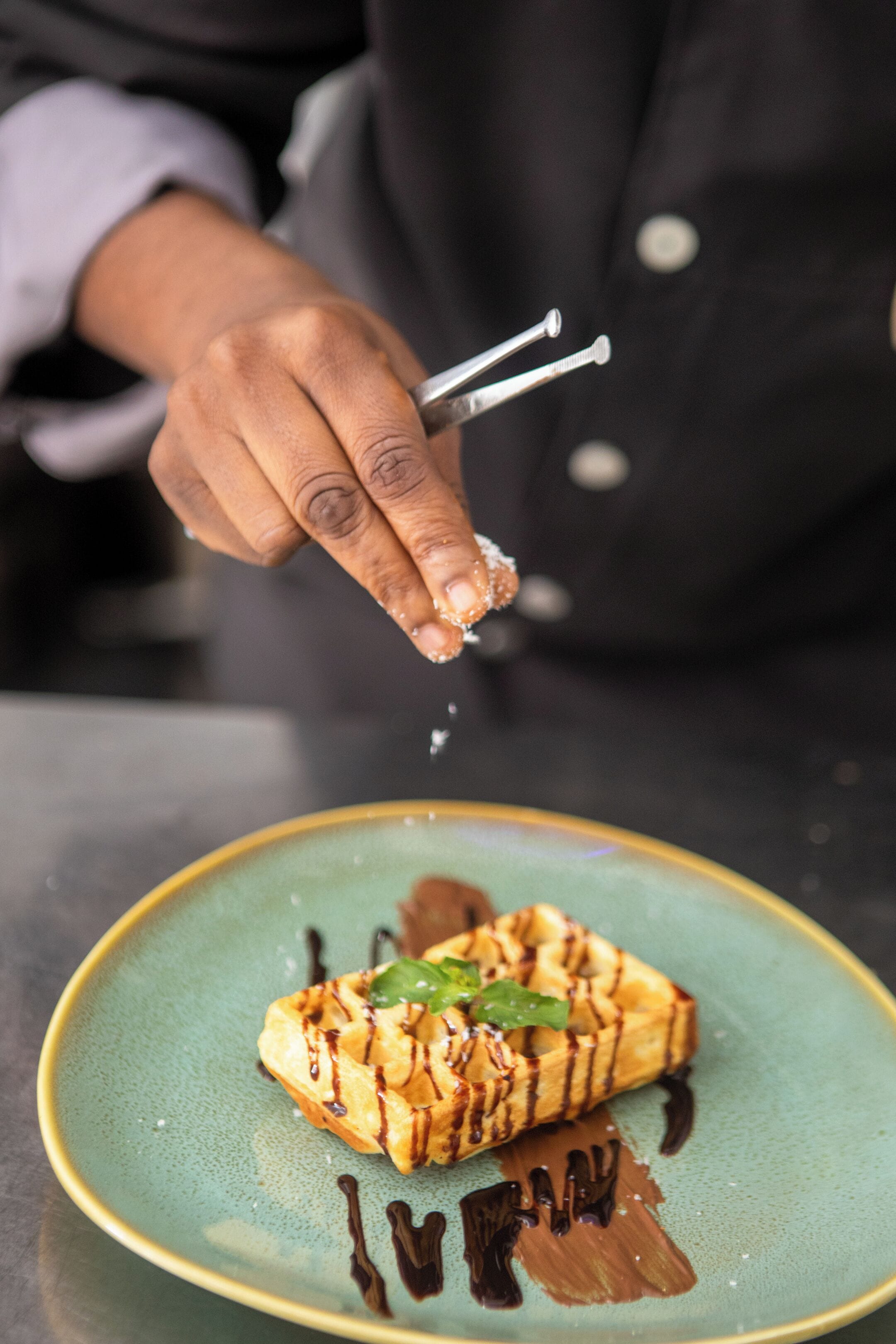 Una mano de chef espolvoreando sal sobre un postre en un plato.