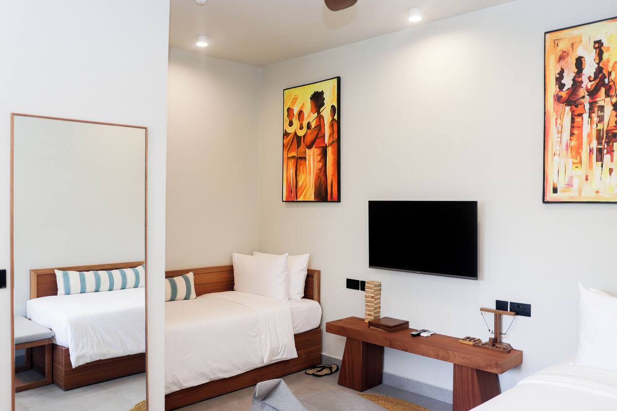 Ein modernes Hotelzimmer mit zwei Betten, einer Holzbank, einem Flachbildfernseher und Kunstwerken an den Wänden.