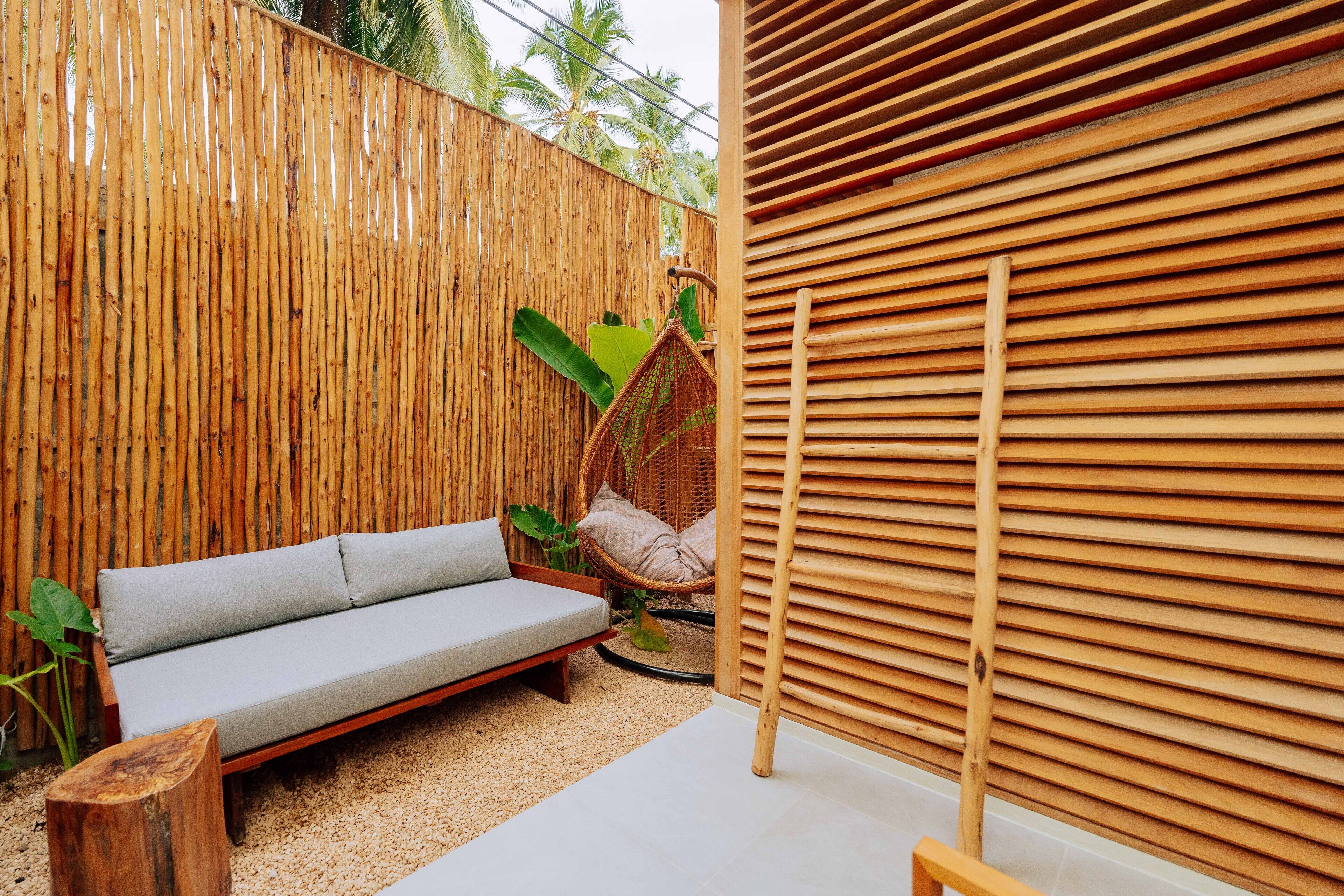 A wooden fence, a wicker chair, a grey sofa, and a wooden slatted wall.