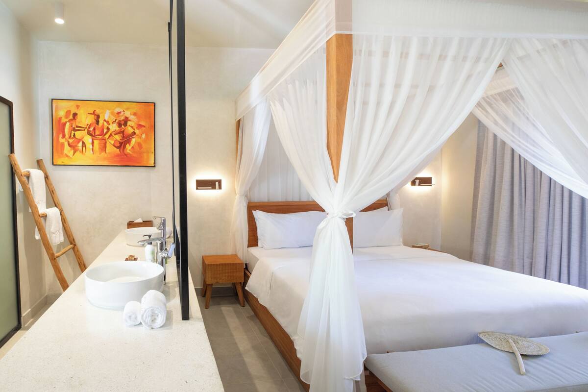 Ein Hotelzimmer mit einem großen Bett, einem Nachttisch, einem kleinen Beistelltisch, einem runden Waschbecken, einem Spiegel und einem Bild an der Wand.