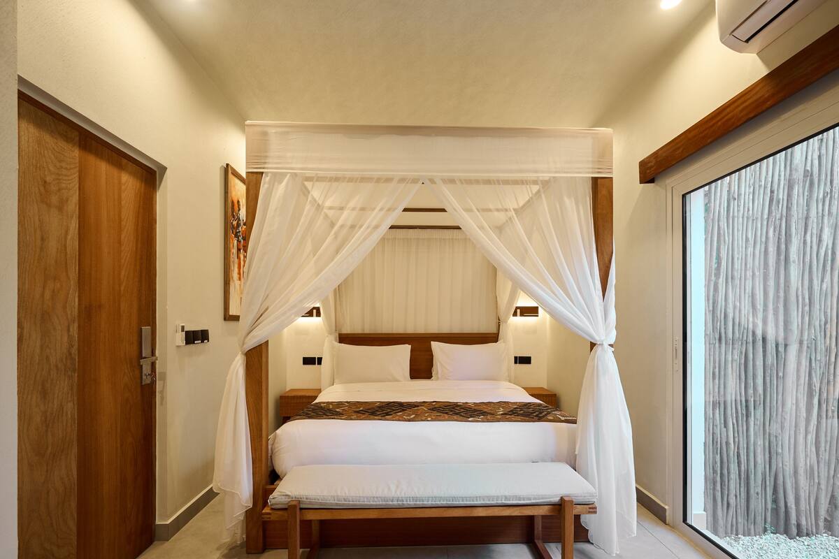 Ein Schlafzimmer mit Himmelbett, Holz-Kopfstück, Nachttischen und einem großen Fenster mit Ausblick.