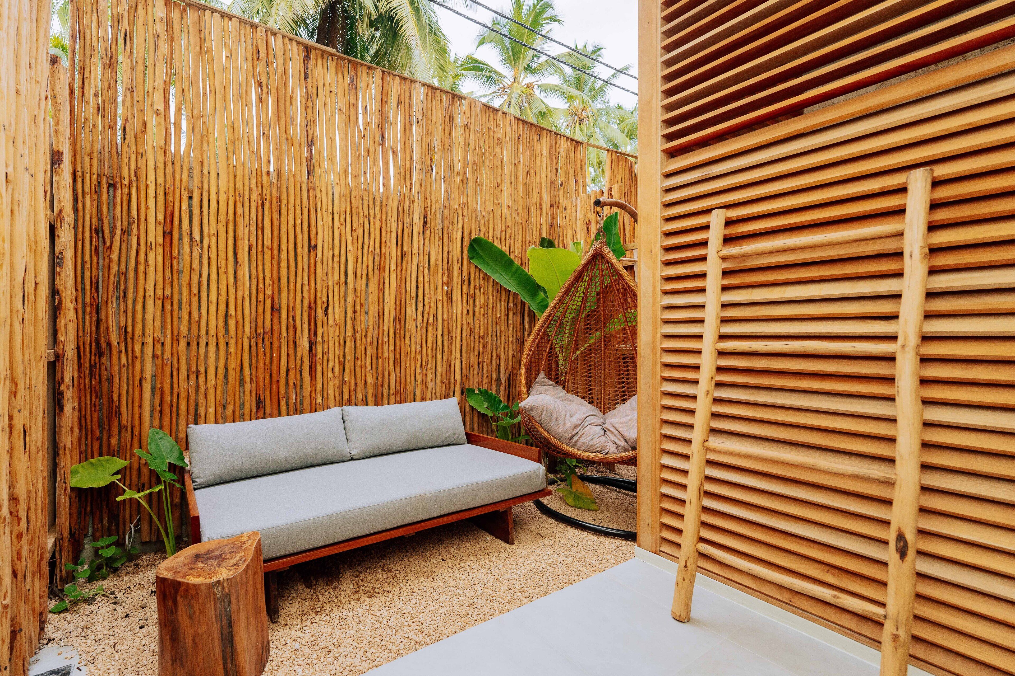 Una valla de bambú, una silla de mimbre y un sofá en un jardín.