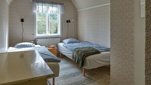 Une chambre avec deux lits simples, une petite table, un radiateur et une fenêtre donnant sur des arbres.