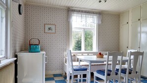 Une pièce avec un radiateur blanc, une table blanche et des chaises bleues, une fenêtre donnant sur un paysage verdoyant et un mur à motifs.