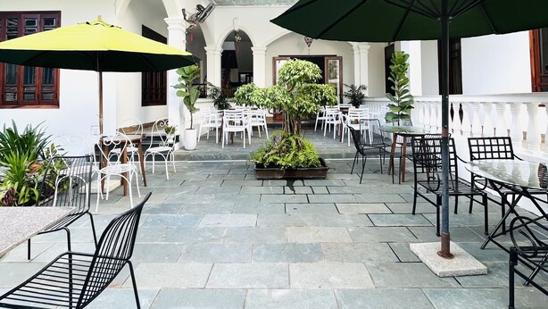 Un patio con mesas al aire libre, plantas en macetas y una fuente central.
