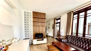 Una sala de estar con piso de madera, un sofá de cuero, un televisor sobre un mueble de madera y un separador de ambientes con diseño.