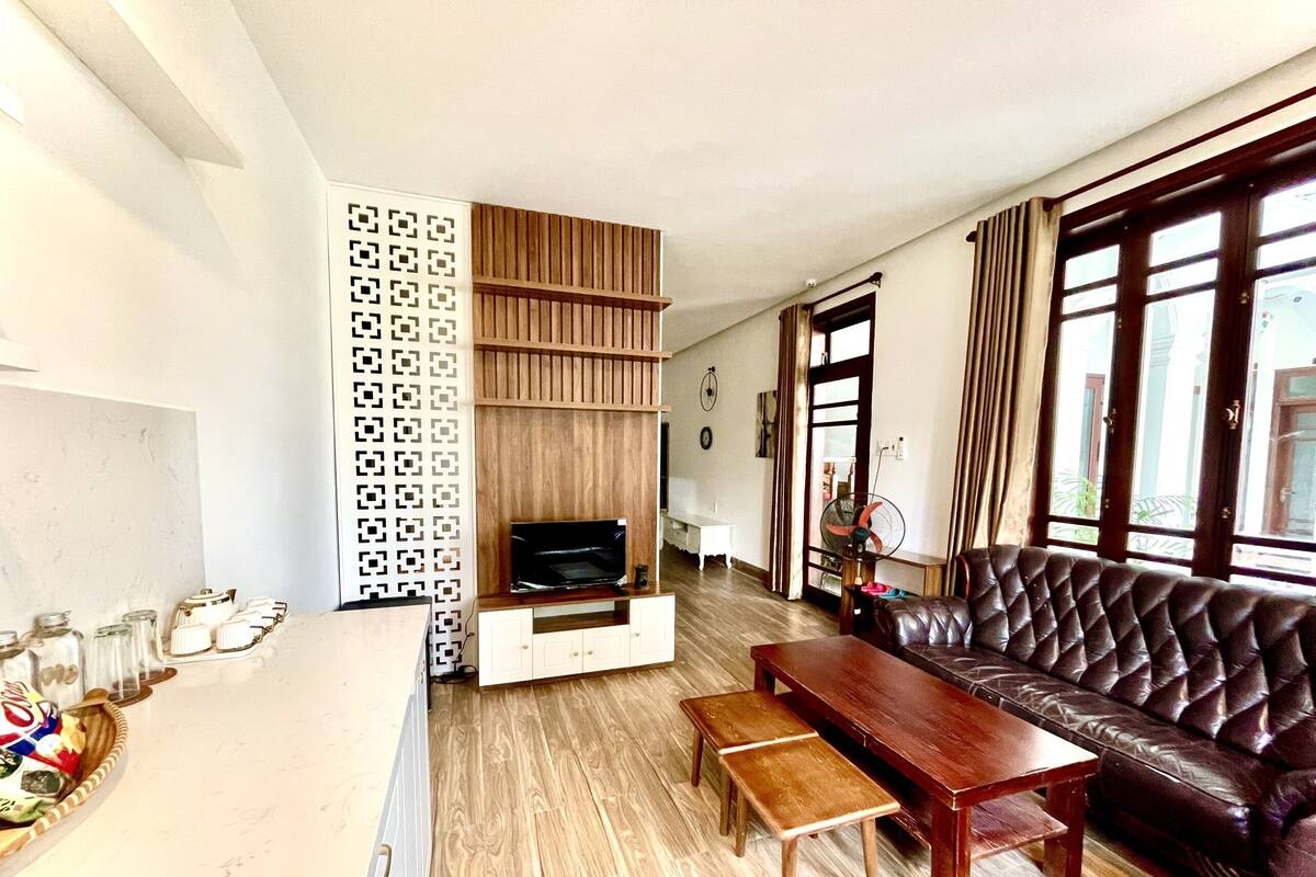 Ein Wohnzimmer mit Holzboden, einer Ledersofa, einem Fernseher auf einem Holzbodenständer und einem Wandteiler mit Muster.
