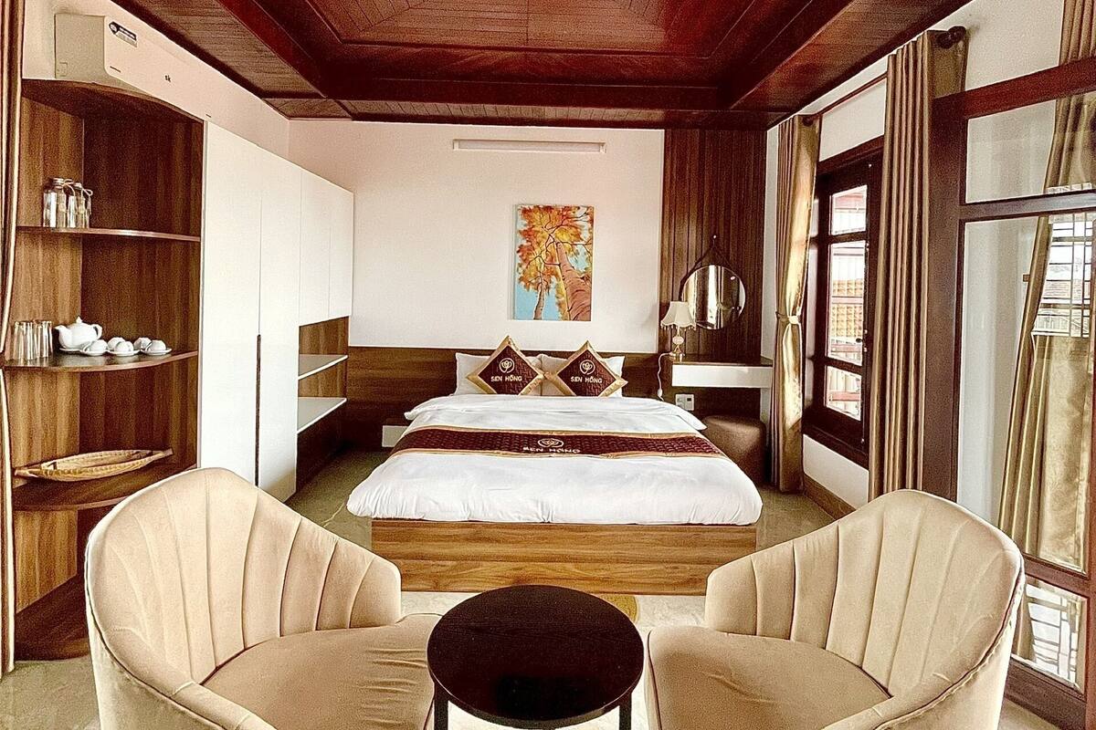 Ein Hotelzimmer mit einem großen Bett, zwei Sesseln, einem kleinen Tisch, Holzregalen und einem Gemälde an der Wand.