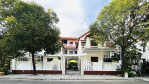 Un edificio de dos pisos con entrada porticada, un balcón en el segundo nivel y cielo despejado.
