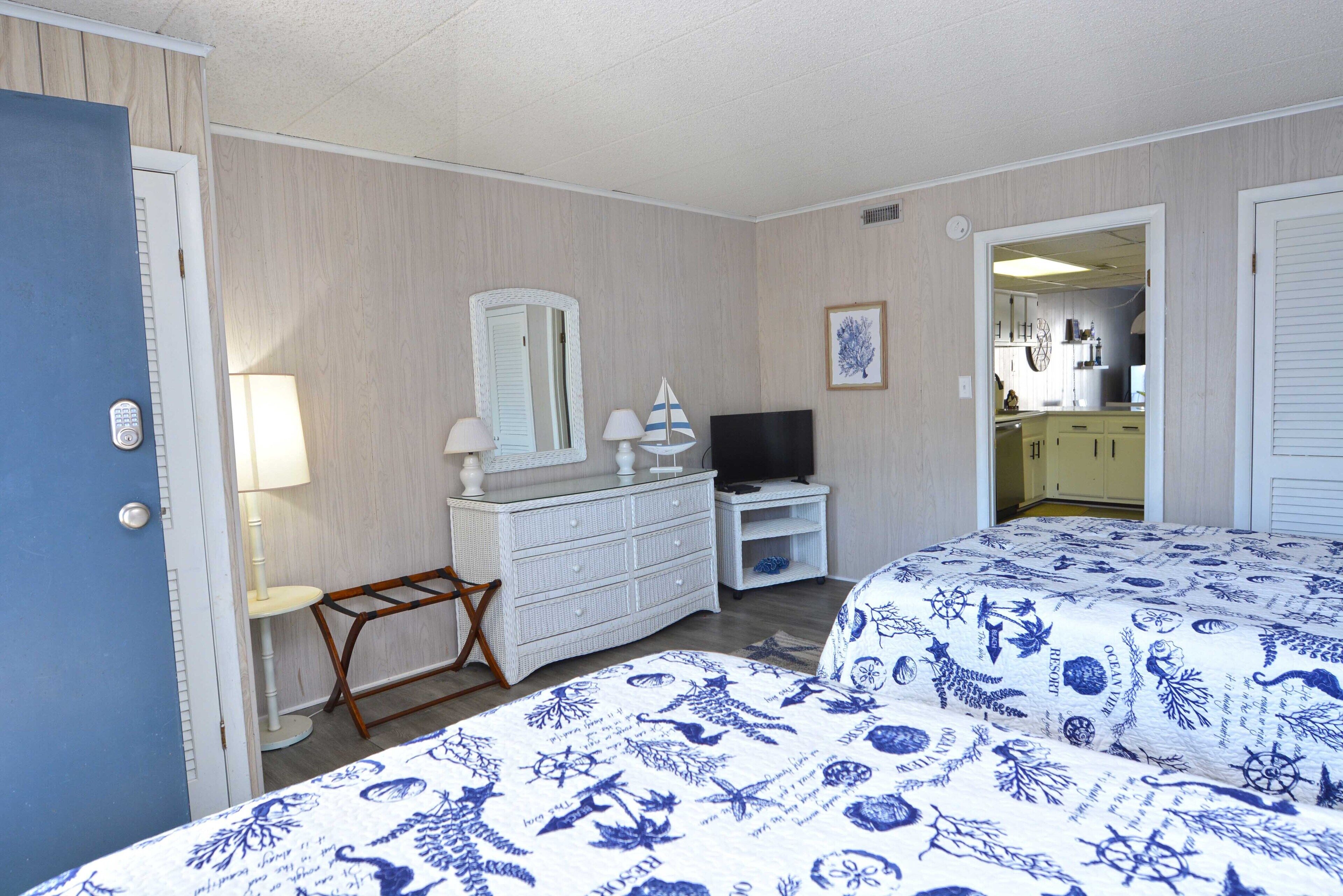 Une chambre d’hôtel avec deux lits, une commode, une télévision et une petite table avec une lampe.