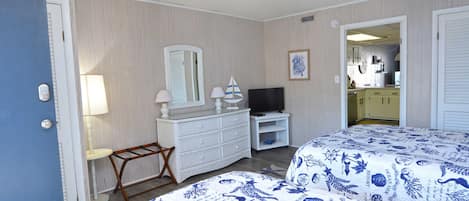 A hotel room with two beds, a dresser, a TV, and a small table with a lamp.