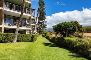 A multi-story hotel with balconies, a well-maintained lawn, and a variety of trees and shrubs.