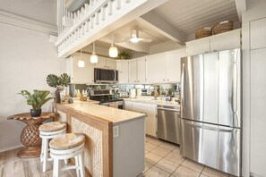 A modern kitchen with a central island, stainless steel appliances, hanging pendant lights, and a staircase leading to an upper level.