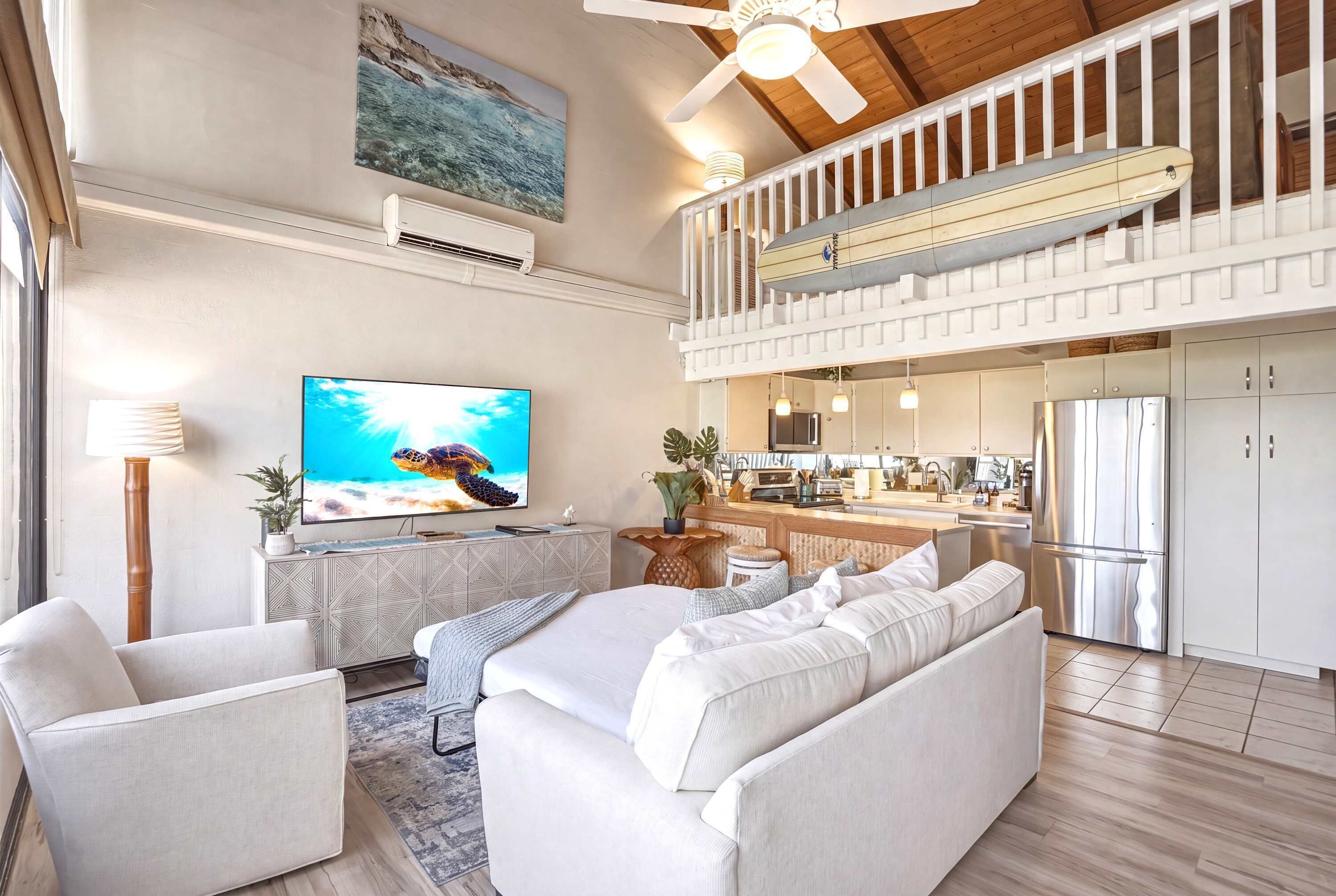 A spacious living area with a large flat-screen TV, a sofa, and a ceiling fan.