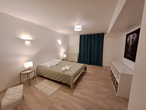 Un dormitorio moderno con cama, lámparas de noche, una mesita pequeña, un banco y un radiador fijado a la pared.
