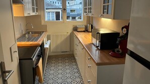 Une petite cuisine avec une fenêtre, un grille-pain, une bouilloire et un appareil rouge posé sur le plan de travail.