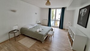 Une chambre moderne avec un grand lit, une table de chevet, une lampe sur pied, un radiateur, une fenêtre avec des rideaux et une œuvre d’art représentant un éléphant accrochée au mur.