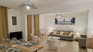 Un salon moderne avec une table à manger en bois, dressée pour quatre personnes, un canapé gris agrémenté de coussins, un fauteuil blanc et une table basse.