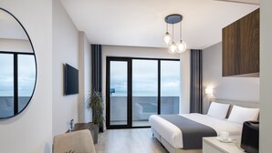 A modern hotel room with a large bed, a desk with a coffee maker, a TV, and a balcony with a view. - STEPS Batumi  Hotel & Suites (Batumi)