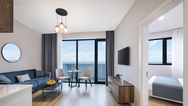 A modern hotel room with a sofa, dining table, chairs, a small kitchen area, and a bed. - STEPS Batumi  Hotel & Suites (Batumi)
