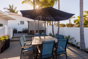 Une terrasse en bois avec une table et des chaises, un parasol et une clôture blanche.