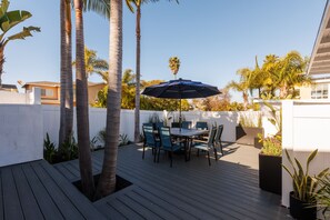 Une terrasse en bois avec une table et des chaises, entourée de palmiers et de plantes en pot.