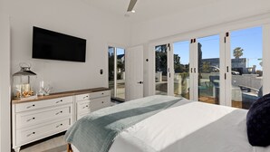 Une chambre à coucher comprenant un lit, un téléviseur fixé au mur, une commode et une porte-fenêtre coulissante donnant sur un espace extérieur.