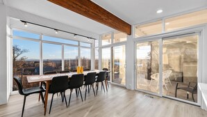 Une pièce spacieuse avec une grande table et des chaises, de grandes fenêtres et une vue sur l’extérieur.