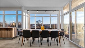 Un espace de restauration moderne, doté d’une grande table, de chaises noires et offrant une vue sur la ville grâce à de larges fenêtres.
