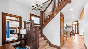 A wooden staircase with a chandelier, a dining area with chairs, and a kitchen with a microwave. - Historic Whittier Neighborhood - Near City Park & Golf - Fenced Yard (Denver)