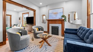 A modern living room with a fireplace, a television, and a large window. - Historic Whittier Neighborhood - Near City Park & Golf - Fenced Yard (Denver)