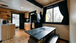 A compact kitchen with wooden cabinetry, a black countertop, and a large window with black curtains. - Moose Ridge at The Spot on Buskey Bay of the Pike Chain of Lakes in Iron River, WI (Iron River)