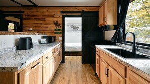 A modern kitchen with wooden cabinetry, a marble countertop, and a large window with a view of trees. - Moose Ridge at The Spot on Buskey Bay of the Pike Chain of Lakes in Iron River, WI (Iron River)