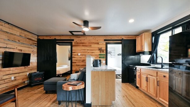 A modern kitchen with wooden cabinetry, a central island, and a dining area with a sofa and coffee table. - Moose Ridge at The Spot on Buskey Bay of the Pike Chain of Lakes in Iron River, WI (Iron River)